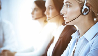 Çağrı merkezi ve iş adamları konsepti. Kulaklıklı, müşterilere danışan güzel bir iş kadını. Ofiste çalışan çeşitli telefon operatörleri.