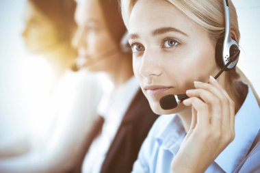 Çağrı merkezi ve iş adamları konsepti. Kulaklıklı, müşterilere danışan güzel bir iş kadını. Ofiste çalışan çeşitli telefon operatörleri.