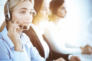 Çağrı merkezi ve iş adamları konsepti. Kulaklıklı, müşterilere danışan güzel bir iş kadını. Ofiste çalışan çeşitli telefon operatörleri.