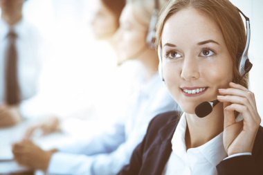 Çağrı merkezi ve iş adamları konsepti. Kulaklıklı, müşterilere danışan güzel bir iş kadını. Ofiste çalışan çeşitli telefon operatörleri.