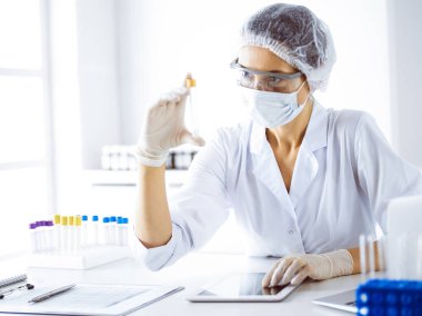 Koruyucu gözlüklü profesyonel kadın bilim adamı laboratuarda reaktörlerle araştırma tüpü kullanıyor. Tıp ve bilim araştırmaları kavramları.