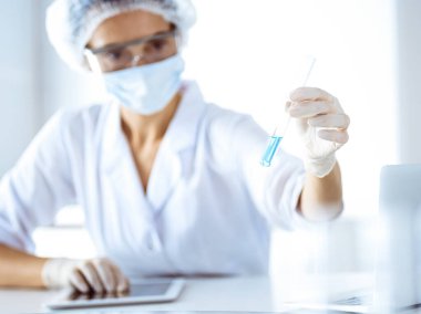 Koruyucu gözlüklü profesyonel kadın bilim adamı laboratuarda reaktörlerle araştırma tüpü kullanıyor. Tıp ve bilim araştırmaları kavramları.