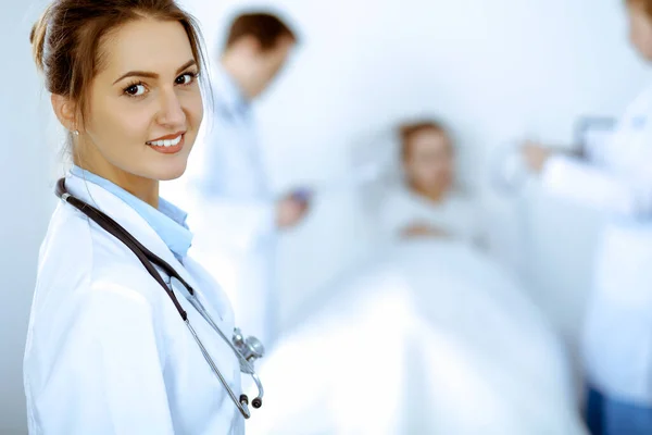 Female doctor smiling on the background with patient in the bed and two doctors