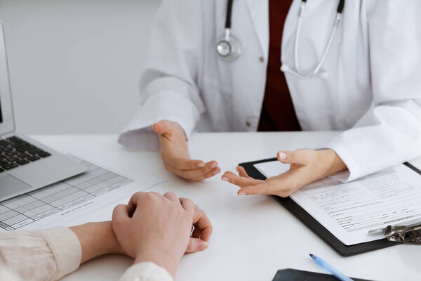 Unknown woman-doctor and patient discussing something while sitting at the table in clinic, close-up. Medicine concept.