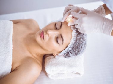 Güzellik uzmanı güneşli spa merkezinde genç esmer bir kadının yüzüne şırıngayla güzellik prosedürü uyguluyor. Kozmetik ilaç ve ameliyat, güzellik iğneleri.