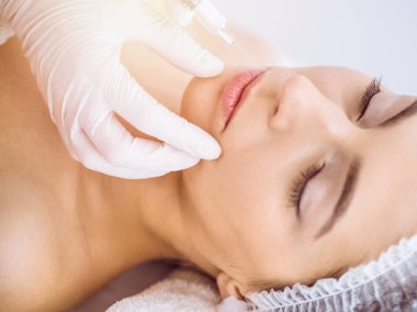 Güzellik uzmanı güneşli spa merkezinde genç esmer bir kadının yüzüne şırıngayla güzellik prosedürü uyguluyor. Kozmetik ilaç ve ameliyat, güzellik iğneleri.