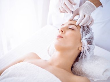 Güzellik uzmanı güneşli spa merkezinde genç esmer bir kadının yüzüne şırıngayla güzellik prosedürü uyguluyor. Kozmetik ilaç ve ameliyat, güzellik iğneleri.