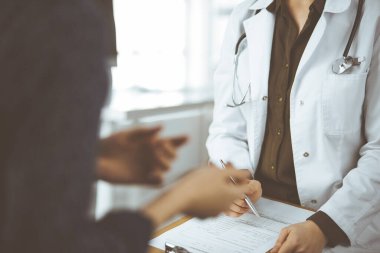 Doktor ve hasta klinikte otururken sağlık muayenesini tartışıyorlar. Hastanede mükemmel bir tıbbi hizmet..