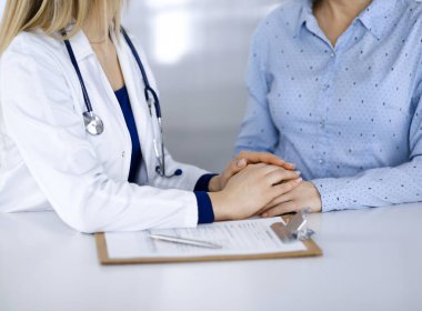 Bilinmeyen kadın doktor, bir klinikteki dolapta yan yana otururken hastasının güvenini tazelemek için elini tutuyor. Kadın hekim, yakın plan bir pano ve steteskop kullanıyor. Hastanede mükemmel bir tıbbi hizmet. Medici.