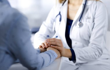 Bilinmeyen kadın-doktor, klinikteki masada birlikte otururken hastaya güven vermek için hastasının elini tutuyor ve mevcut sağlık muayenesini tartışıyor. Steteskopu olan bir kadın doktor, yakın plan. Mükemmel. 