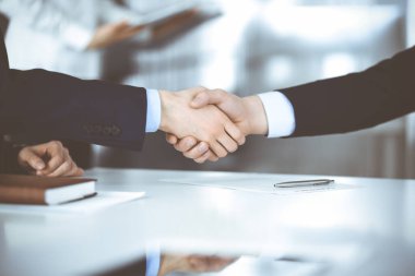 İş adamları toplantıda ya da pazarlıkta el sıkışıyor, yakın plan. Bilinmeyen iş adamları grubu ve modern bir ofiste arka planda bir kadın. Takım çalışması, ortaklık ve el sıkışma kavramı.