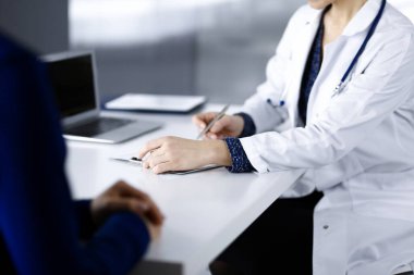 Bilinmeyen kadın-doktor, bir klinikteki dolapta birlikte otururken hastasına bazı tıbbi tavsiyeler yazıyor. Hekim bir dosya kullanıyor, yakın plan. Hastanede mükemmel bir tıbbi hizmet. Tıp konsepti.