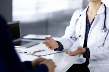 Bilinmeyen kadın-doktor, klinikteki dolapta birlikte otururken hastasıyla teşhisi hakkında konuşuyor. İşyerindeki doktor, yakın plan. Hastanede mükemmel bir tıbbi hizmet. Tıp konsepti.