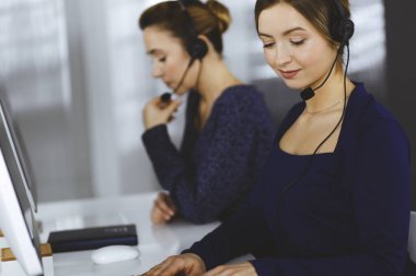 İki iş kadını, modern bir ofiste masada otururken müşterilerle kulaklıkla sohbet ediyorlar. Çağrı merkezinde çeşitli insanlar. Tele pazarlama ve müşteri hizmetleri