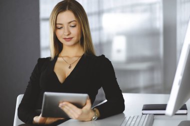 Başarılı genç iş kadını firmasının kabinesinde çalışırken bir bilgisayar tableti kullanıyor. Ofisteki masada oturan bir sekreterin resmi ya da portresi.