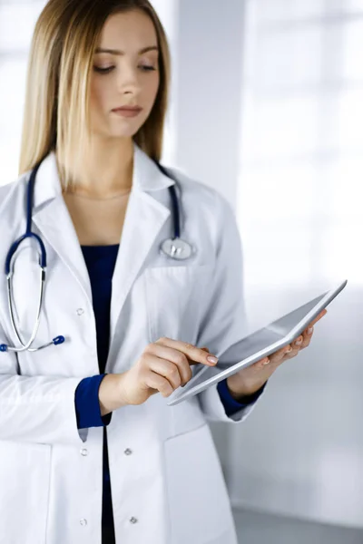 젊은 전문 여성 과 의사가 진료소에 서 있는 동안 태블릿 컴퓨터를 사용하고 있습니다. 아름다운 여성 의사가 활동하는 모습. 병원에서의 완벽 한 의료 서비스. 의학적 개념 — 스톡 사진