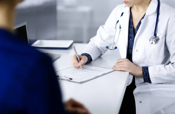 Bilinmeyen kadın-doktor, bir klinikteki dolapta birlikte otururken hastasına bazı tıbbi tavsiyeler yazıyor. Hekim bir dosya kullanıyor, yakın plan. Mükemmel.