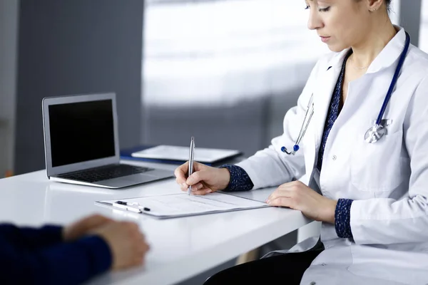 Ismeretlen nő-orvos ír néhány orvosi ajánlást a betegének, miközben együtt ülnek az asztalnál a szekrényben egy klinikán. Az orvos írótáblát használ, közelit. Tökéletes. — Stock Fotó