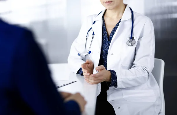 Mulher-médica desconhecida está conversando com seu paciente sobre seu diagnóstico, enquanto sentados juntos na mesa no armário em uma clínica. Médico no local de trabalho, close-up. Serviço médico perfeito em um — Fotografia de Stock