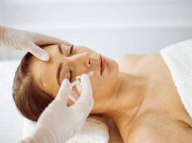 Güzellik uzmanı, genç esmer kadının yüzüne şırıngayla güzellik prosedürü uyguluyor. Kozmetik ilaç ve ameliyat, güzellik iğneleri.