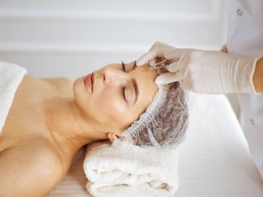 Güzellik uzmanı, genç esmer kadının yüzüne şırıngayla güzellik prosedürü uyguluyor. Kozmetik ilaç ve ameliyat, güzellik iğneleri.