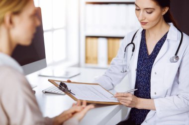 Neşeli gülümseyen kadın doktor ve hasta kadın güncel sağlık muayenesini güneşli klinikte otururken tartışıyorlar. Tıp konsepti