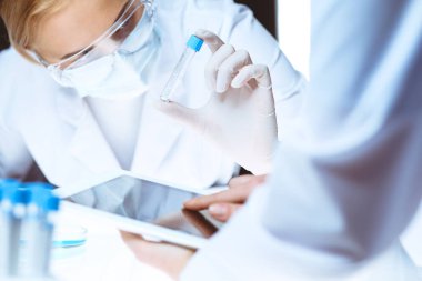 Koronavirüs salgını. Koruyucu gözlüklü profesyonel kadın bilim adamı laboratuarda reaktörlerle araştırma tüpü kullanıyor. İlaç ve virüs koruması kavramları.