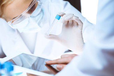 Koronavirüs salgını. Koruyucu gözlüklü profesyonel kadın bilim adamı laboratuarda reaktörlerle araştırma tüpü kullanıyor. İlaç ve virüs koruması kavramları.