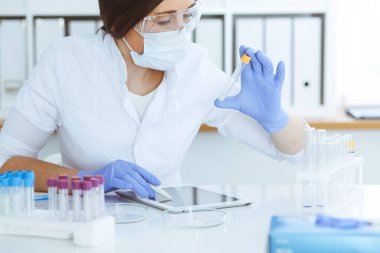 Koruyucu gözlüklü profesyonel kadın bilim adamının laboratuvarda reaksiyonlarla ya da kan testiyle deney yapması. Tıp, biyoteknoloji ve araştırma konsepti.