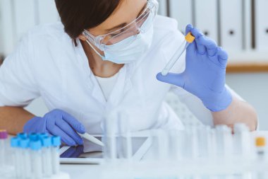 Koruyucu gözlüklü profesyonel kadın bilim adamının laboratuvarda reaksiyonlarla ya da kan testiyle deney yapması. Tıp, biyoteknoloji ve araştırma konsepti.
