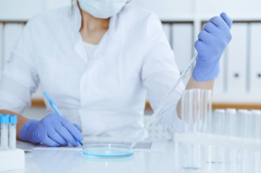 Koruyucu gözlüklü profesyonel kadın bilim adamının laboratuvarda reaksiyonlarla ya da kan testiyle deney yapması. Tıp, biyoteknoloji ve araştırma konsepti.