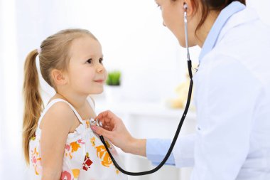 Doktor steteskopla küçük bir kızı muayene ediyor. Her zamanki tıbbi muayenede gülümseyen çocuk hasta. Tıp ve sağlık hizmetleri kavramları