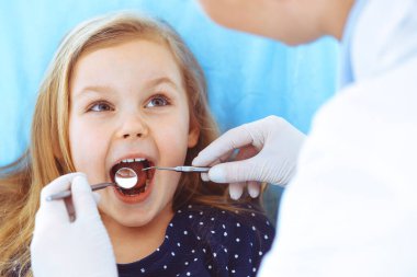 Doktor muayenesi sırasında ağzı açık bir şekilde dişçi koltuğunda oturan küçük kız. Dişçi muayenehanesi. Tıp konsepti. Renkli fotoğraf