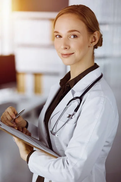 Allegro sorridente medico femminile utilizzando appunti in clinica soleggiata. Ritratto di donna medico amichevole al lavoro. Concetto di medicina — Foto Stock