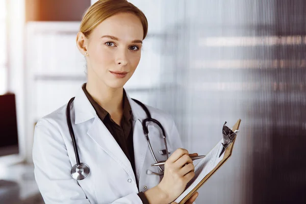 Allegro sorridente medico femminile utilizzando appunti in clinica soleggiata. Ritratto di donna medico amichevole al lavoro. Concetto di medicina — Foto Stock