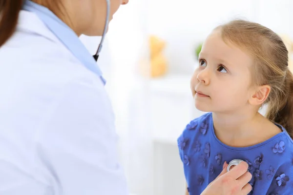 Arzt untersucht ein kleines Mädchen per Stethoskop. Glücklich lächelnder Kinderpatient bei der üblichen ärztlichen Untersuchung. Medizin- und Gesundheitskonzepte — Stockfoto