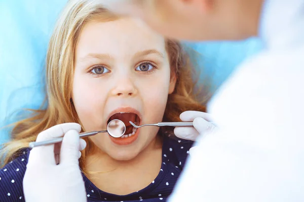 Niña sentada en la silla dental con la boca abierta durante el chequeo oral mientras es doctora. Visita al consultorio del dentista. Concepto de medicina. Foto tonificada — Foto de Stock