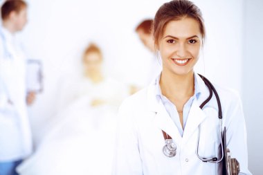 Arka planda gülümseyen kadın doktor, yatakta hasta ve iki doktor.