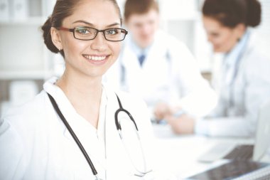 Mutlu gülümseyen kadın doktor tıbbi personelle toplantıda oturup kameraya bakıyor. Tıp konsepti