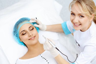 Kadın yüzüne kaş dövmesi yapan profesyonel bir güzellik uzmanı. Güzellik salonunda kalıcı kaş makyajı, yakın çekim. Kozmetoloji tedavisi