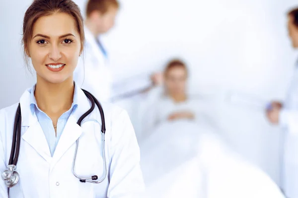 Female doctor smiling on the background with patient in the bed and two doctors