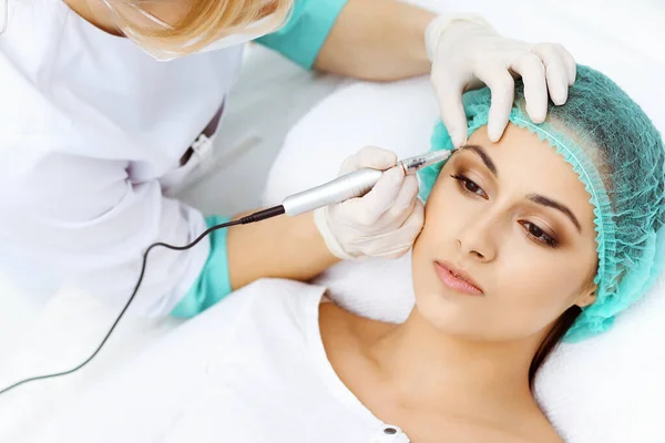 Professionele schoonheidsspecialiste die wenkbrauwtatoeage doet op vrouwengezicht. Permanente make-up in schoonheidssalon, close-up. Cosmetologische behandeling — Stockfoto