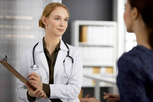 Freundlich lächelnde Ärztin und Patientin diskutieren im Sitzen in der Klinik über die aktuelle Gesundheitsuntersuchung. Medizin und Gesundheitskonzept — Stockfoto