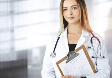 Genç iyimser kadın-doktor güneşli bir klinikte dururken elinde bir pano tutuyor. Dost canlısı, steteskoplu bir kadın doktorun portresi. Hastanede mükemmel bir tıbbi hizmet.