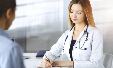 Bilinmeyen kadın-doktor, bir klinikteki güneşli dolapta birlikte otururken hastasına bazı tıbbi tavsiyeler yazıyor. Doktor bir pano kullanıyor, yakın plan.