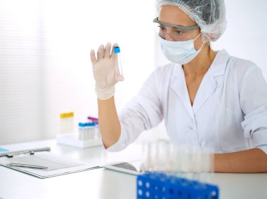 Koruyucu gözlüklü profesyonel kadın bilim adamı laboratuarda reaktörlerle araştırma tüpü kullanıyor. Tıp ve araştırma kavramları