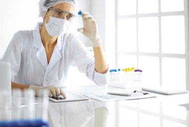 Koruyucu gözlüklü profesyonel kadın bilim adamı laboratuarda reaktörlerle araştırma tüpü kullanıyor. Tıp ve araştırma kavramları