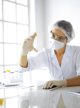 Koruyucu gözlüklü profesyonel kadın bilim adamı laboratuarda reaktörlerle araştırma tüpü kullanıyor. Tıp ve araştırma kavramları