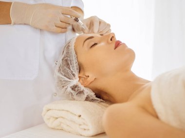 Güzel bir kadın kapalı gözlerle güzellik iğneleri yaptırıyor. Güzellik uzmanı elleri şırıngayla kadın yüzüne güzellik prosedürü uyguluyor. Kozmetik tıp ve cerrahi konsepti