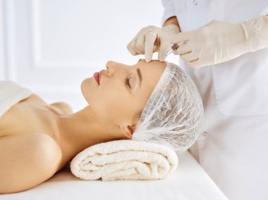 Güzel bir kadın kapalı gözlerle güzellik iğneleri yaptırıyor. Güzellik uzmanı elleri şırıngayla kadın yüzüne güzellik prosedürü uyguluyor. Kozmetik tıp ve cerrahi konsepti